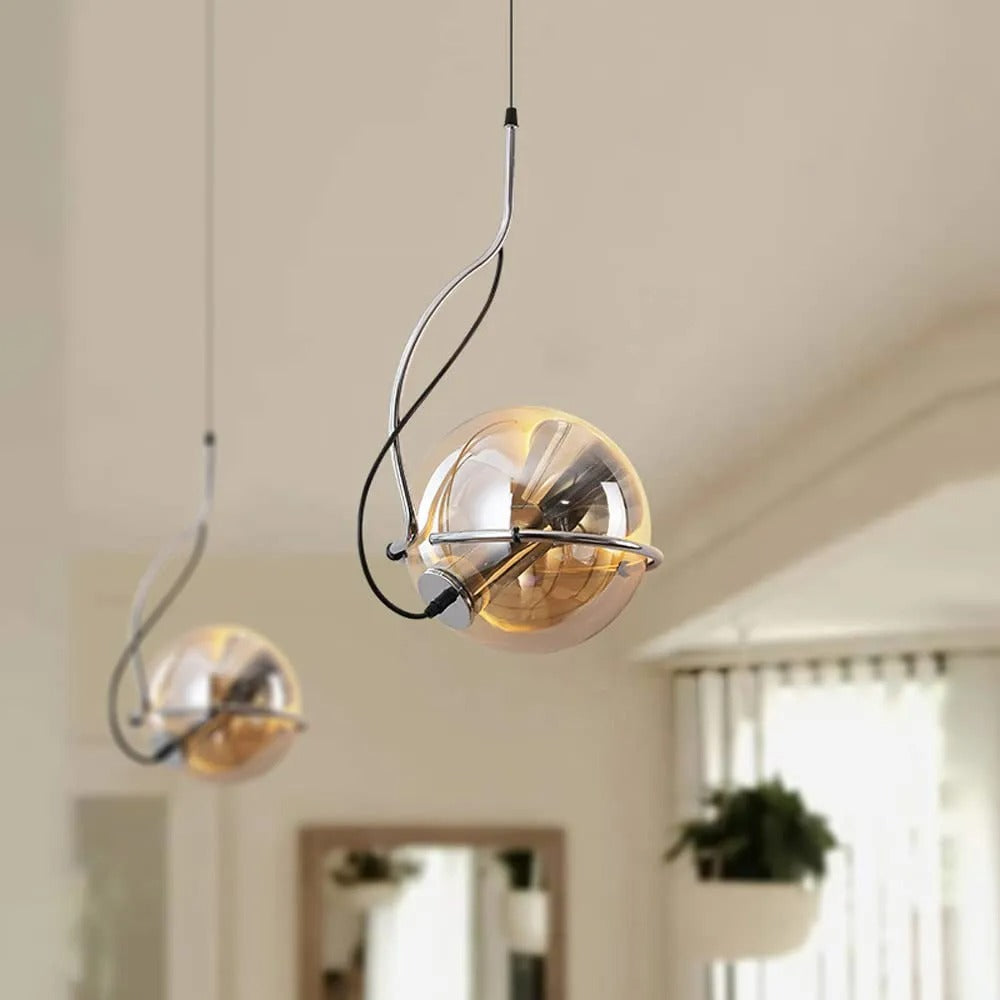 Two Clérachic Amber Glass Dome Pendant Lights hang at staggered heights beside a window and a hanging plant.