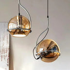 A pair of Clérachic Amber Glass Dome Pendant Lights at staggered heights, one lit and one off beside wall art.