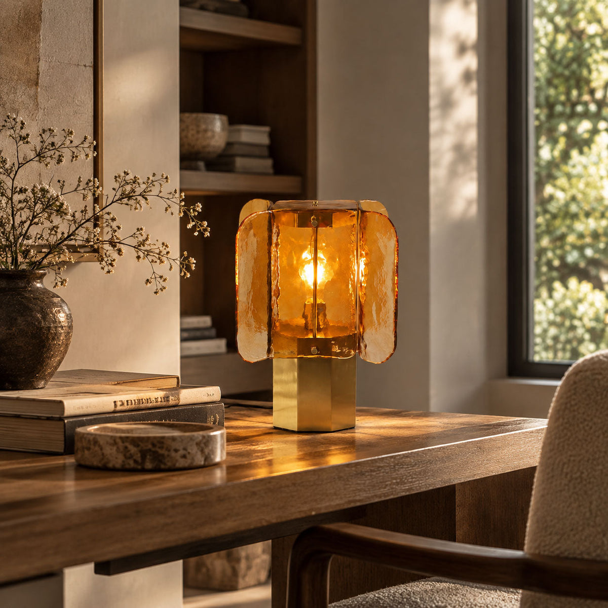 Lit amber Clérachic table lamp with a brass base on a walnut desk, beside a shelf and a vase of dried stems in low sun.