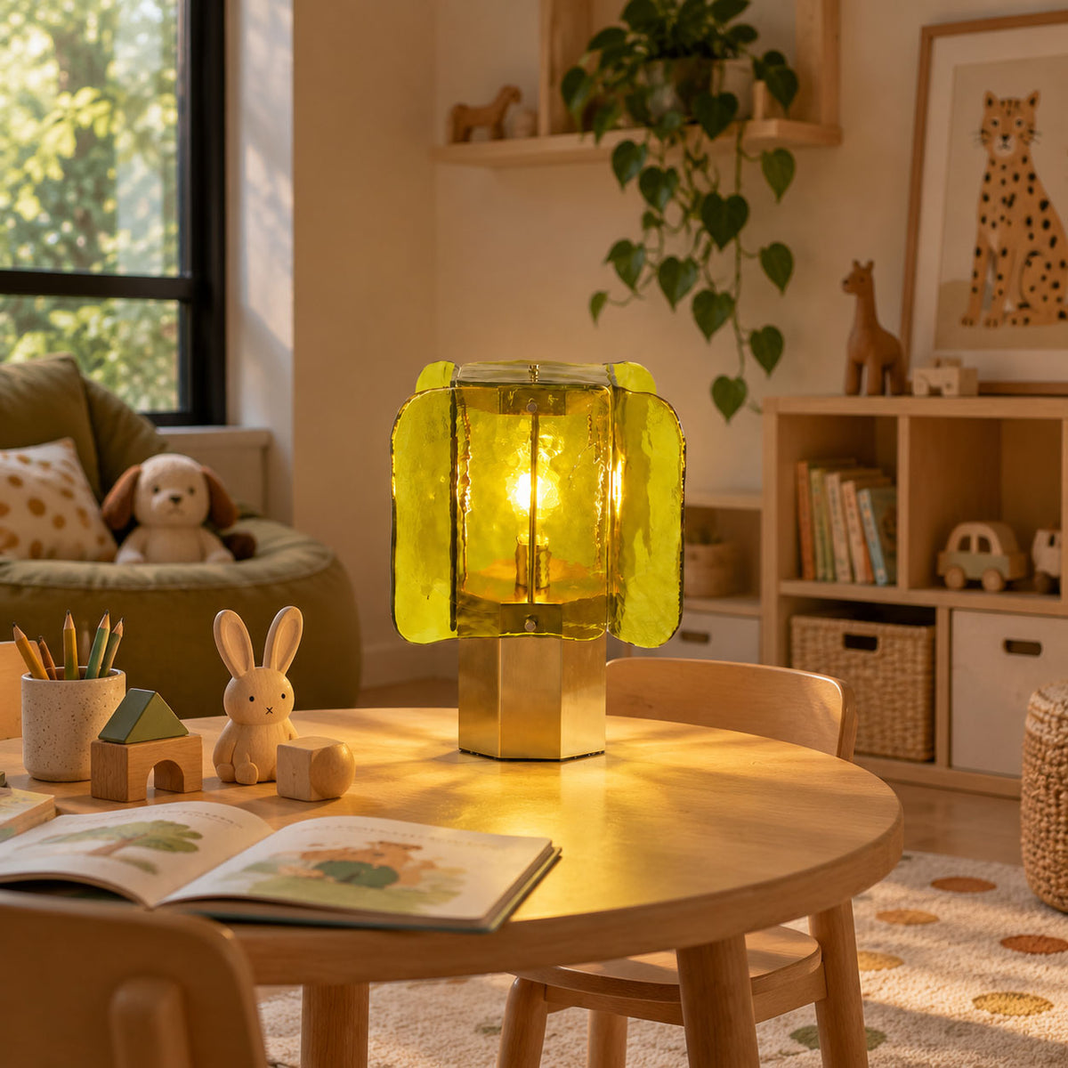 Green and gold Clérachic table lamp glowing on a round wooden children's table, with a picture book and a toy rabbit beside it.