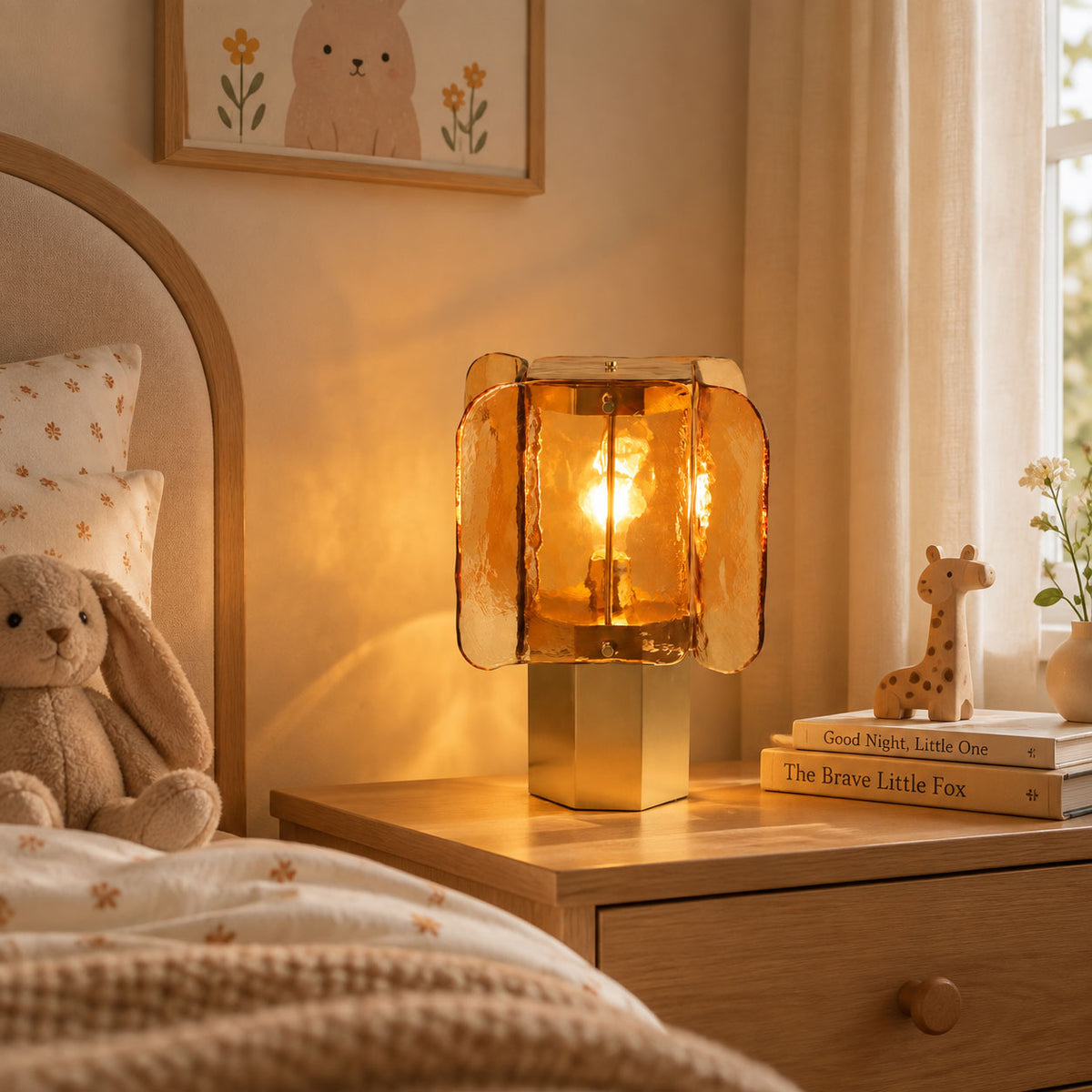 Amber glass Clérachic table lamp on a wooden bedside chest, with a toy giraffe, stacked books and a cream curtain behind.