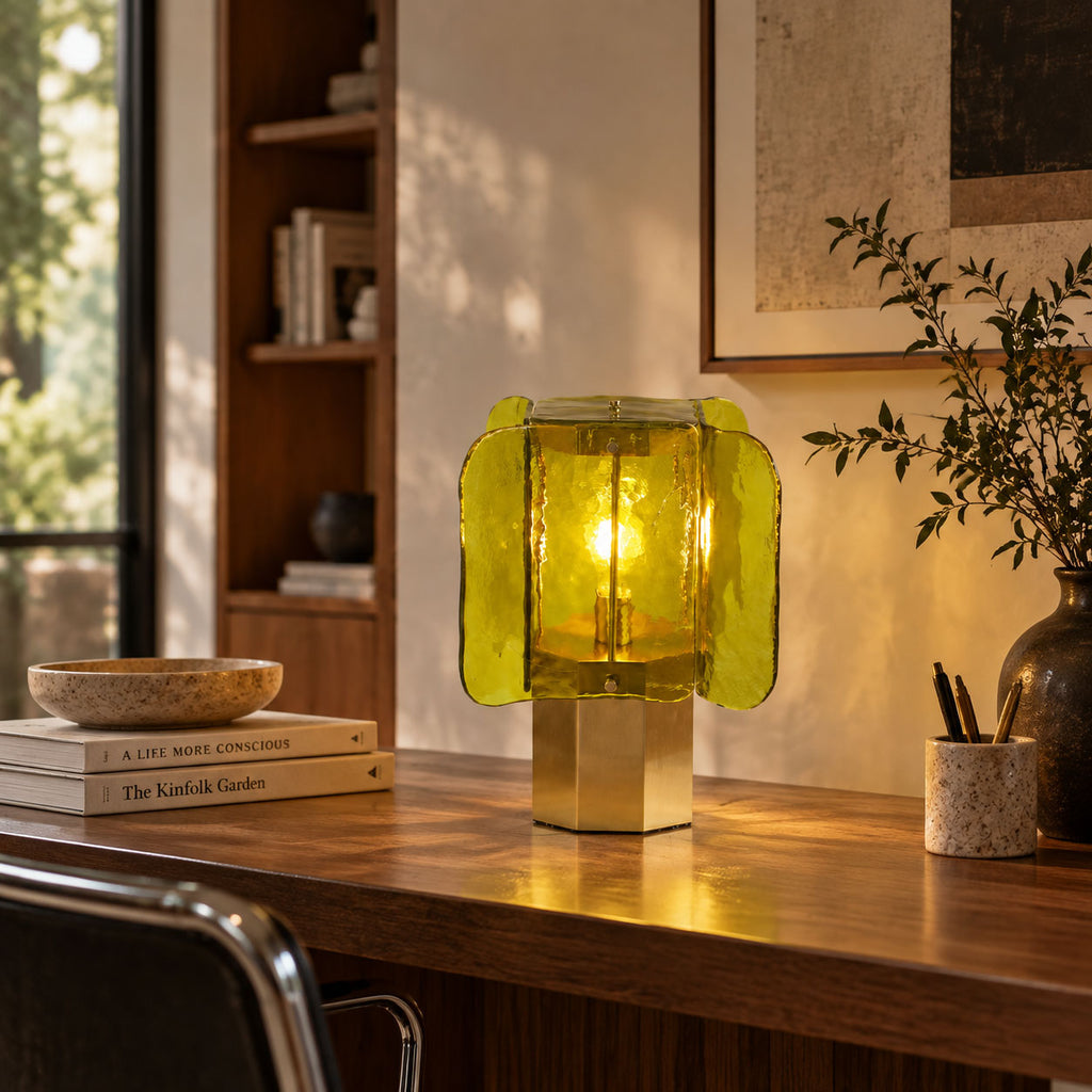 Green-glass Clérachic table lamp on a wooden desk by a pen pot and stacked books, with a leafy plant and shelving behind.