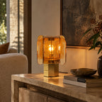 Amber Clérachic table lamp lit on a stone-topped console, next to a stone bowl and books, under a large abstract painting.