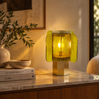 Green glass Clérachic table lamp glowing on a marble-topped cabinet, with olive stems in a vase and a stack of books.