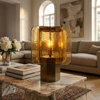 Amber glass Clérachic table lamp on a marble coffee table, with art books and white peonies, in front of a cream sofa.