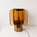 Amber and gold Clérachic table lamp with four curved glass panels, set on a white surface with its cord trailing behind.