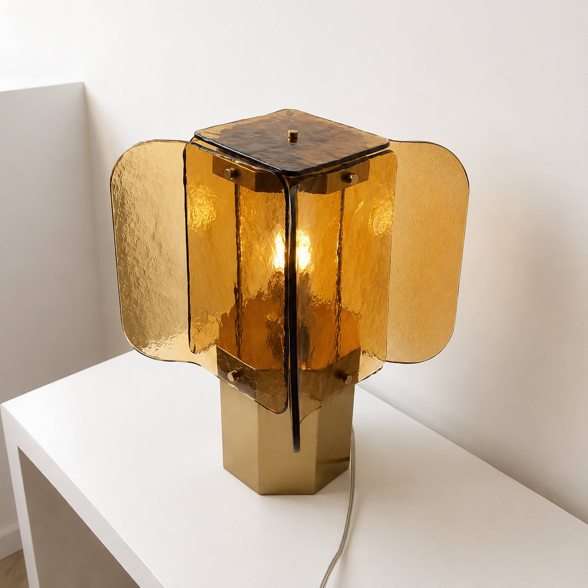 Three-quarter view of this Clérachic table lamp, its wavy amber panels fanned out above the brass octagonal base on a white shelf.