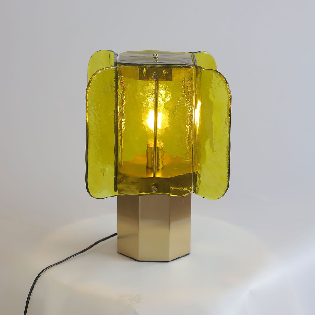 Green glass Clérachic table lamp lit on a draped white surface, with a black cord trailing from the brass base.