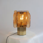 Amber glass Clérachic table lamp lit on a draped white surface, with a black cord trailing from the brass octagonal base.