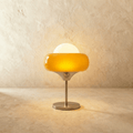 Clérachic table lamp lit on a limewash surface, an amber glass ring shade under a white opal dome on a slim chrome stem.