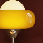 Close view of the Clérachic lamp's glossy amber glass ring, white opal dome and polished chrome trumpet collar on a dark wall.