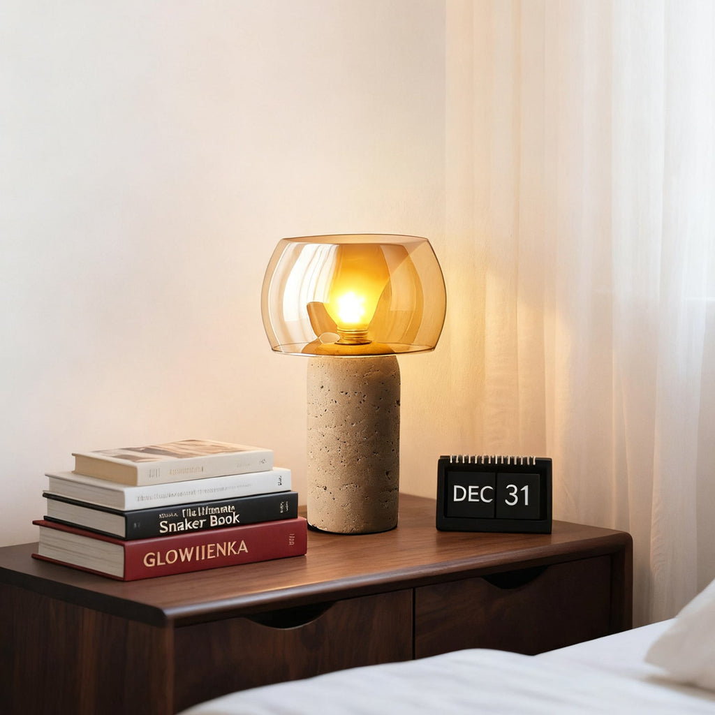 This Clérachic travertine table lamp glowing amber on a walnut bedside chest, next to a stack of books and a flip calendar.