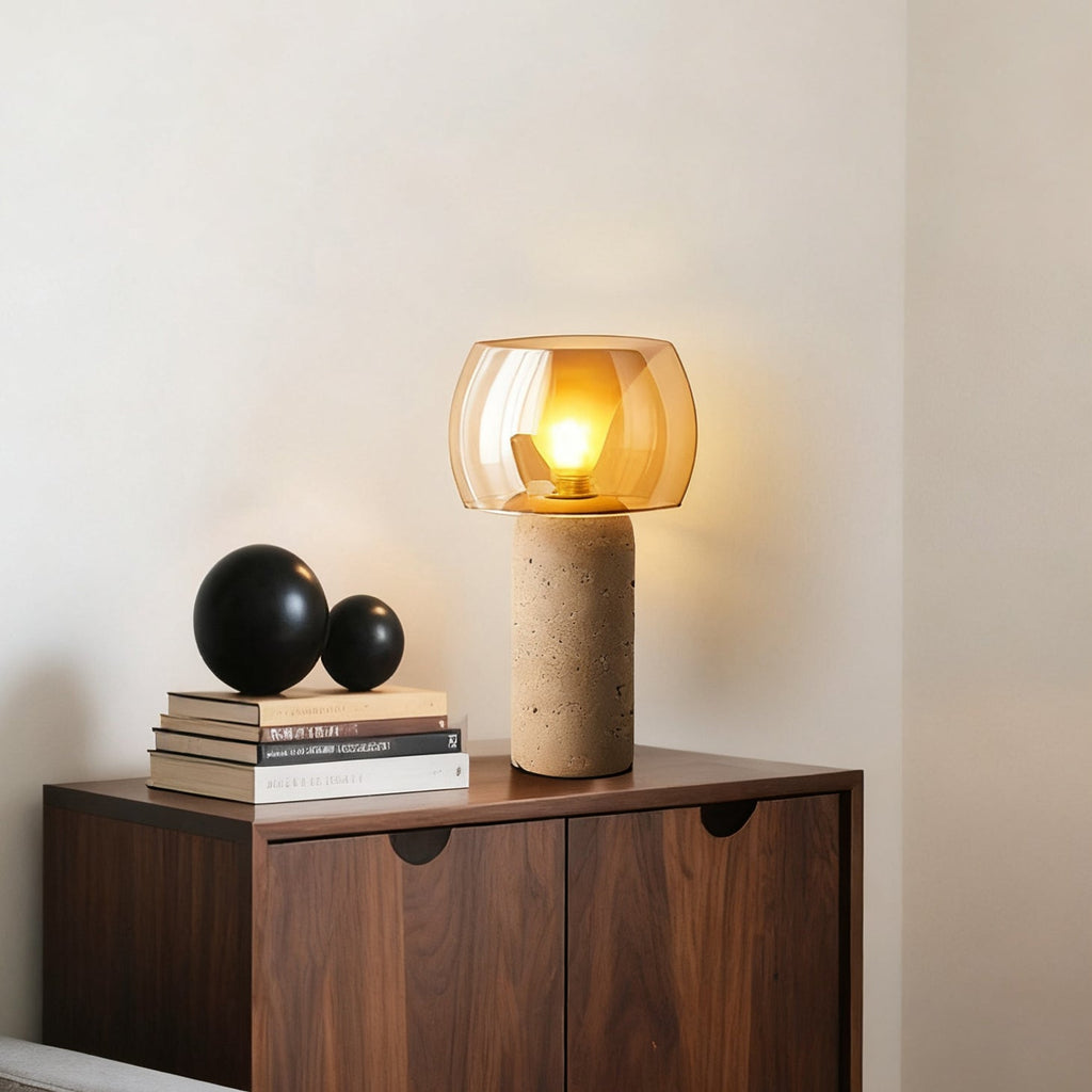 Beside a stack of books and two black spheres on a walnut cabinet, a Clérachic table lamp lights its amber glass shade.