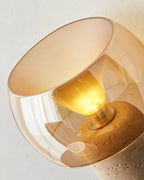 Close view of the amber glass shade and the bulb on this Clérachic lamp, with the pitted travertine base tilting in from below.