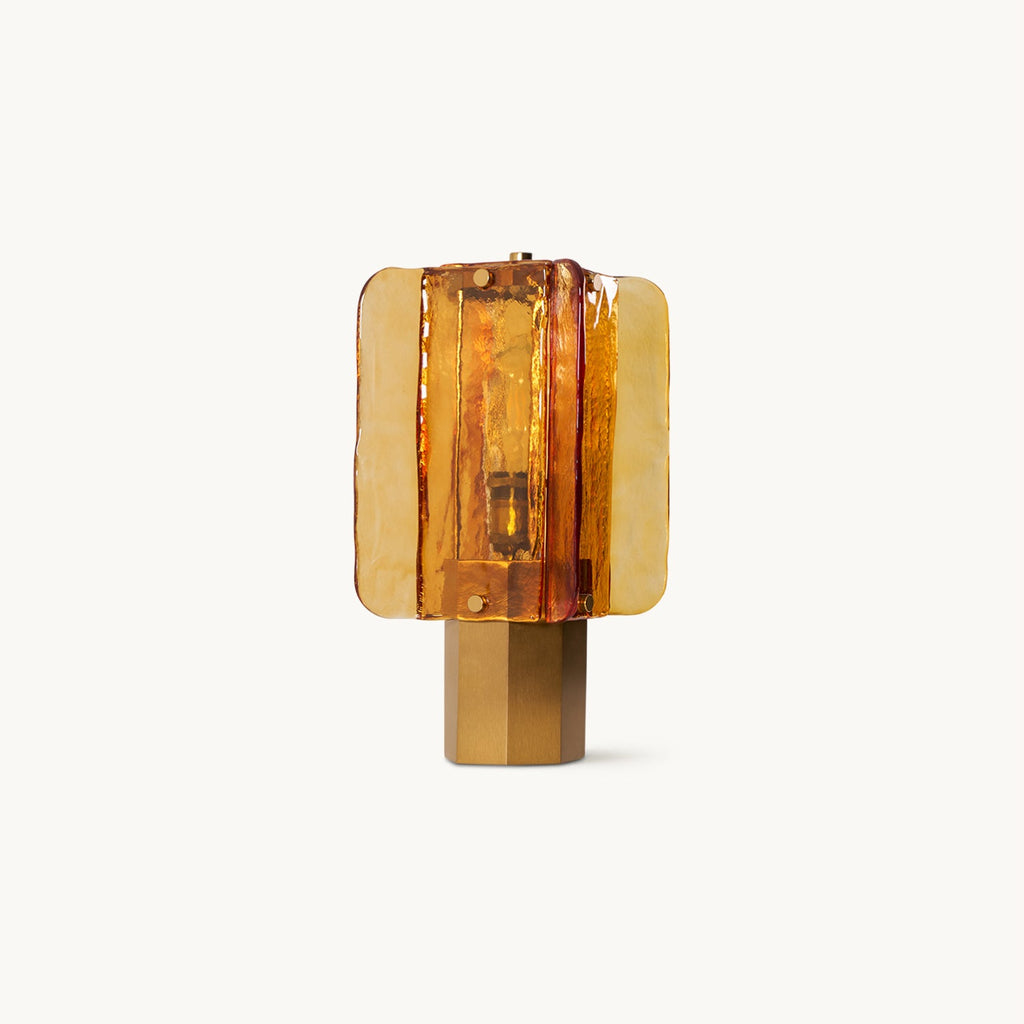 A Clérachic table lamp on a plain white backdrop, with amber glass panels fanned around a lit bulb on a six-sided metal base.