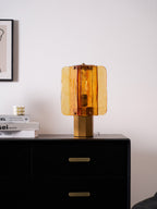 A small Clérachic table lamp lit in amber on a black two-drawer chest, with a framed print on the wall behind it.