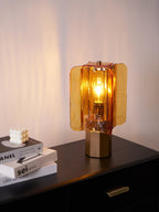 Light from this Clérachic table lamp spills up a pink-tinged wall, its amber glass panels bright above a black sideboard top.