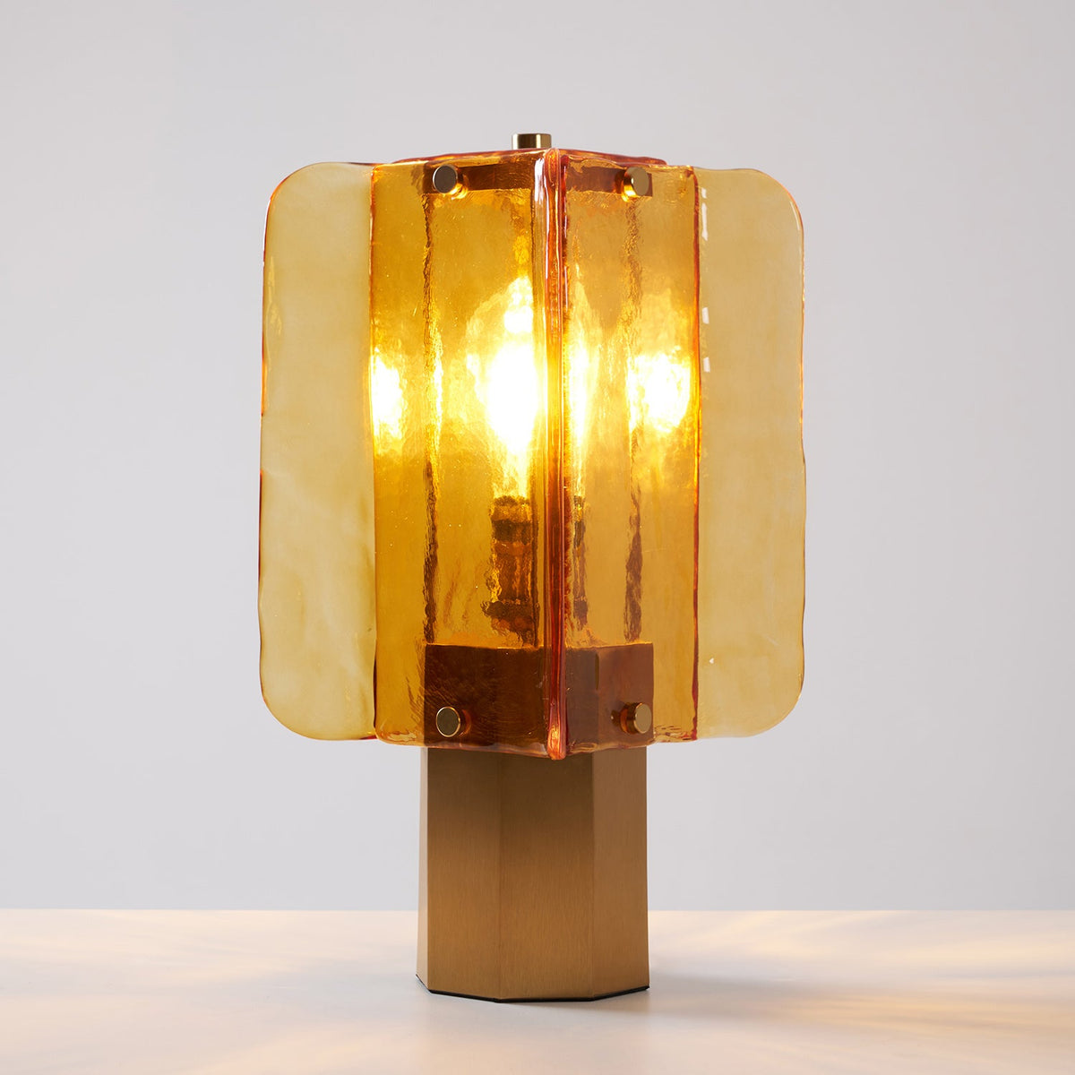 Close view of the textured amber glass panels and brass-coloured studs on this Clérachic table lamp, lit on a pale surface.