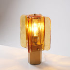 Close three-quarter view of this Clérachic table lamp, with the bulb glowing inside rippled amber glass above a six-sided base.