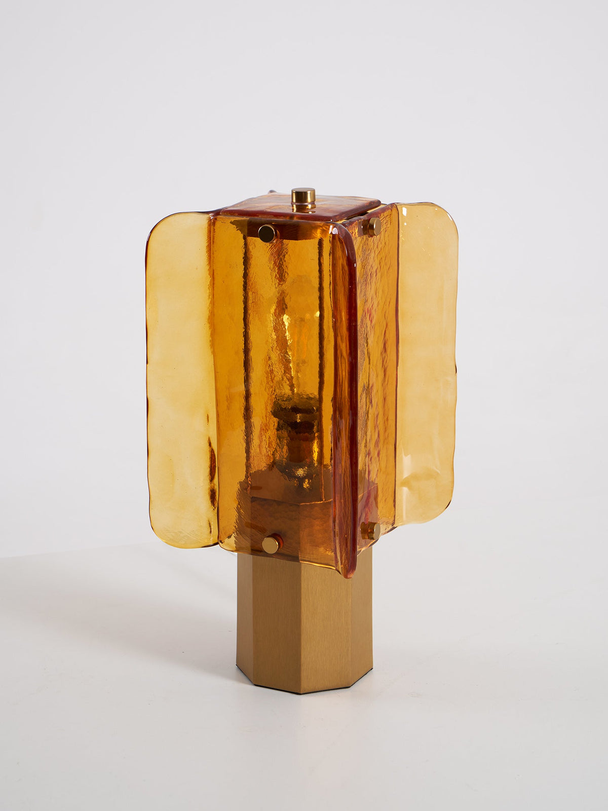 Clérachic table lamp unlit against a grey backdrop, the amber glass panels in front of a bulb above a plain metal base.