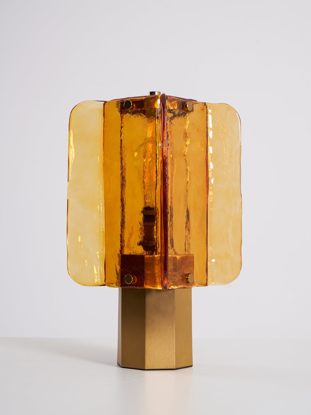 Front view of this unlit Clérachic table lamp on a pale floor, with studded amber glass panels and a brushed metal base.