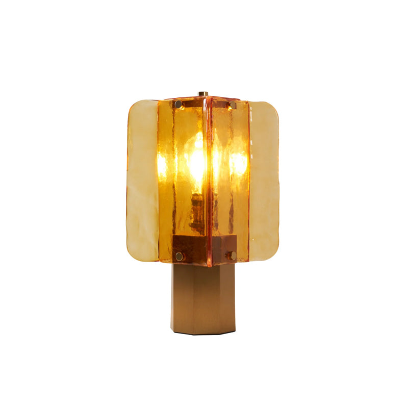 Cut-out view of this Clérachic table lamp lit on white, with its amber glass panels glowing above the six-sided metal base.