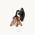 This Clérachic wall lamp on a plain white backdrop, an amber swirled glass shade on a scrolled red bronze arm and oval backplate.