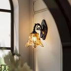 Beside an arched window, a lit Clérachic wall lamp glows warm on a pale wall, its amber glass shade flaring at the rim.