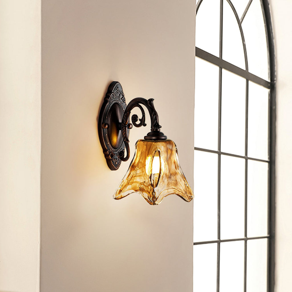 A lit Clérachic wall lamp on a beige wall next to a tall arched window, its amber glass catching the light.