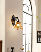 Low in the frame, a lit Clérachic wall lamp sits by an arched window, a black vase and framed picture below.