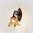 A Clérachic wall lamp lit against a soft white wall, with warm light behind its amber glass and a pitted bronze backplate.