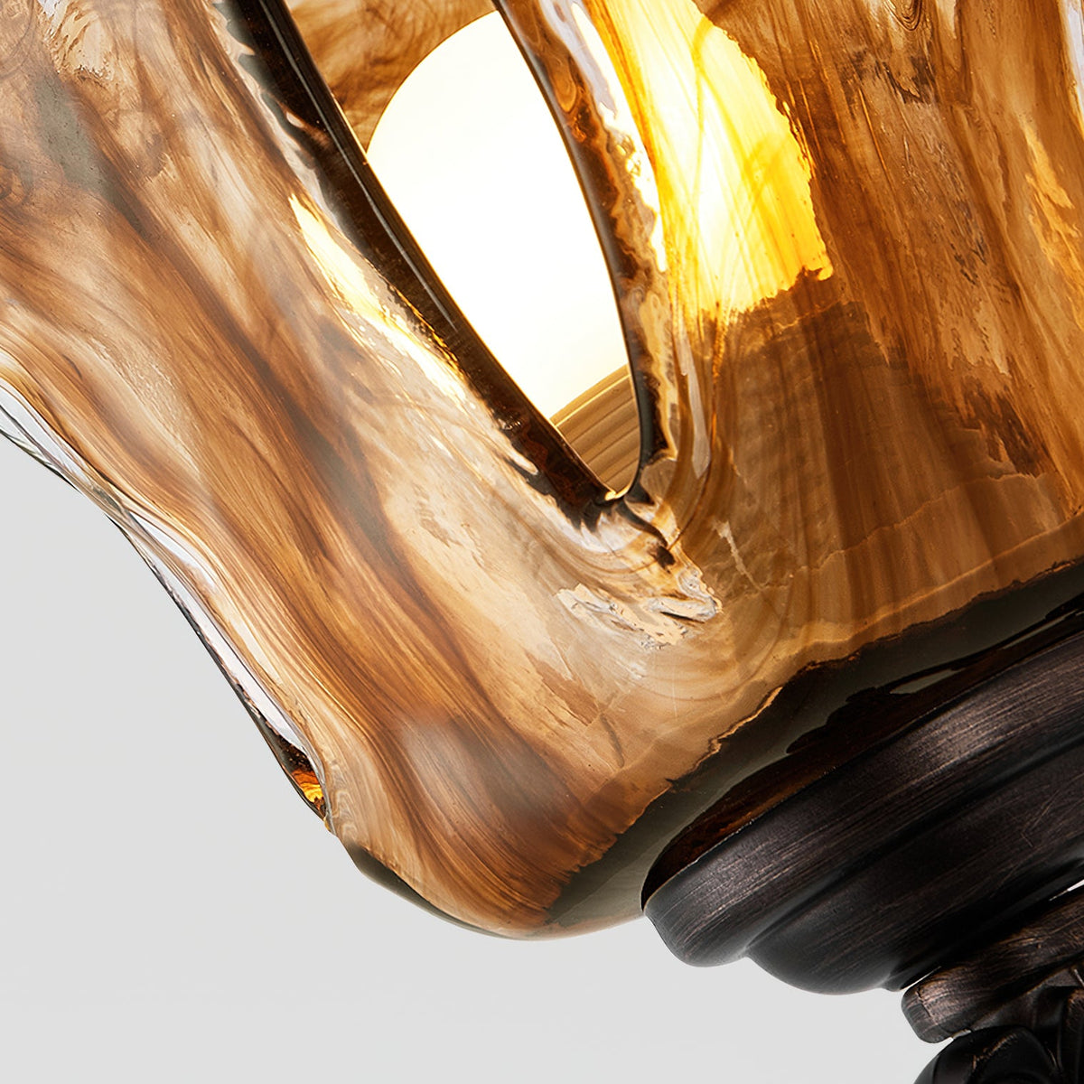 Looking up into this Clérachic wall lamp shade, the lit bulb glows through swirls of amber and brown glass.