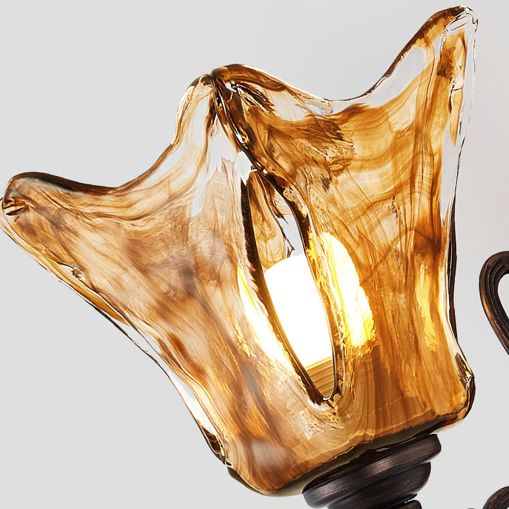 The swirled amber shade of this Clérachic wall lamp, lit, with a split in the glass and the bronze cup above.