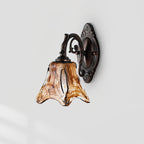 An unlit Clérachic wall lamp on a pale grey wall, its streaked amber glass shade and curled bronze arm in side view.