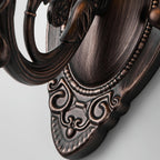 Close view of the oval backplate of this Clérachic wall lamp, with beaded edging and scrolled red bronze detail.