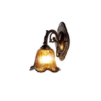 A lit wall lamp with a ribbed amber glass bell shade on an ornate bronze backplate, cut out on a white backdrop, from Clérachic.