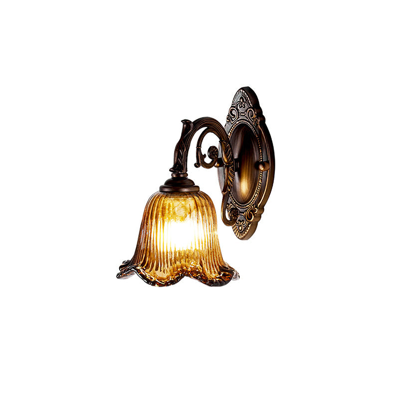 A lit wall lamp with a ribbed amber glass bell shade on an ornate bronze backplate, cut out on a white backdrop, from Clérachic.