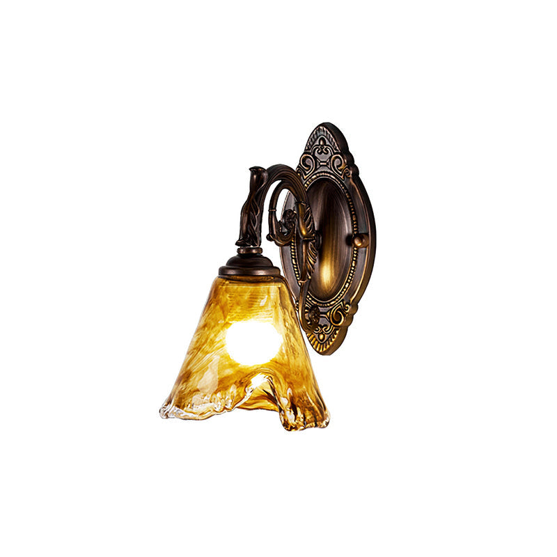 This Clérachic wall lamp on white, lit, with a golden amber flared glass shade, a scrolled arm and an oval bronze backplate.