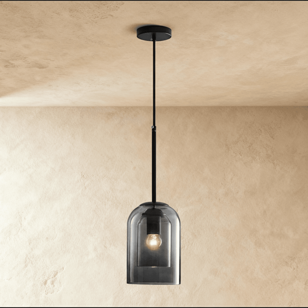 This Clérachic smoky gray glass pendant hangs from a black cord, its bulb glowing warmly inside the dome shade.