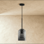 Clérachic's smoky gray glass pendant hangs unlit from a black cord against a plain plaster wall.