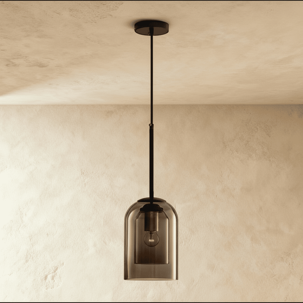 This Clérachic smoky gray glass pendant glows warmly, its dome shade catching light on a plaster wall.