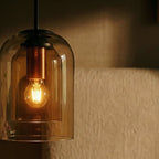 A close view of the Clérachic amber glass pendant shows its nested inner cylinder and glowing bulb.