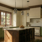 Three Clérachic smoky gray glass pendants hang at staggered heights above a walnut kitchen island.