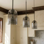 A close view shows three Clérachic smoky gray pendants, each with a nested inner glass cylinder glowing.