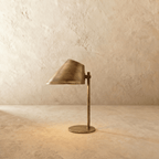 Clérachic table lamp in a warm satin brass finish, an angled cone shade glowing on a slim stem.