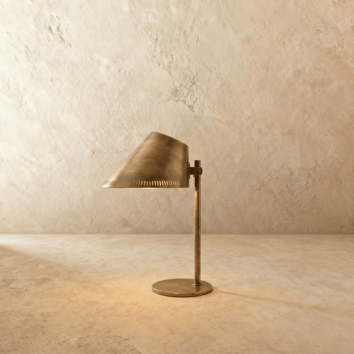 Clérachic table lamp in a warm satin brass finish, an angled cone shade glowing on a slim stem.