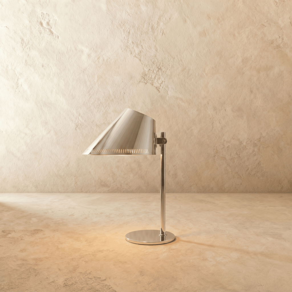 Clérachic table lamp in chrome, an angled cone shade glowing on a slender stem and round base.