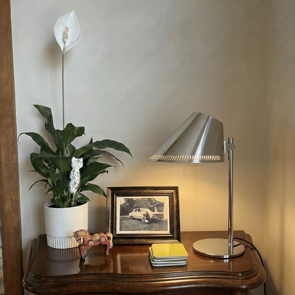 Clérachic table lamp in chrome glowing on a side table beside a framed photo and a peace lily.