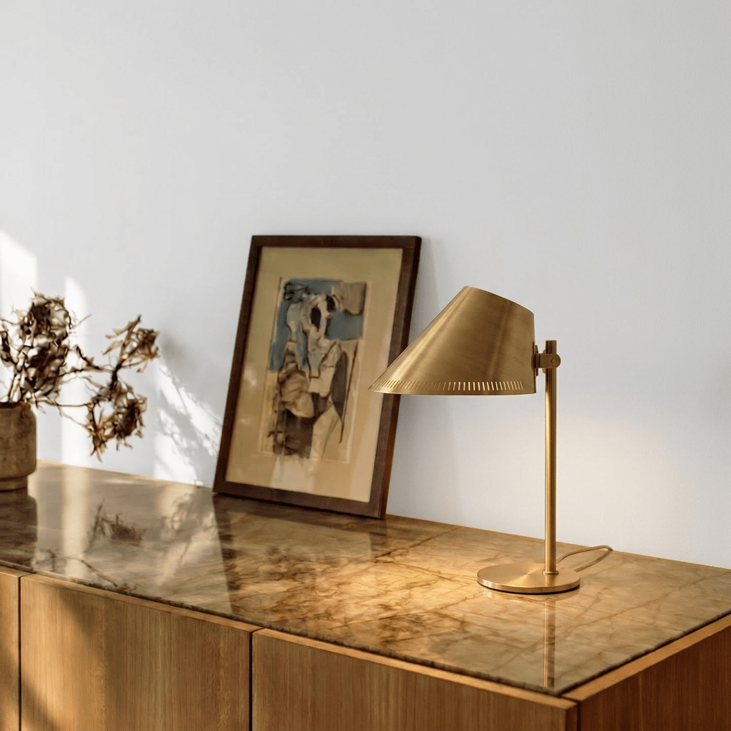 Clérachic table lamp in brass glowing on a marble sideboard beside a framed print and dried branches.