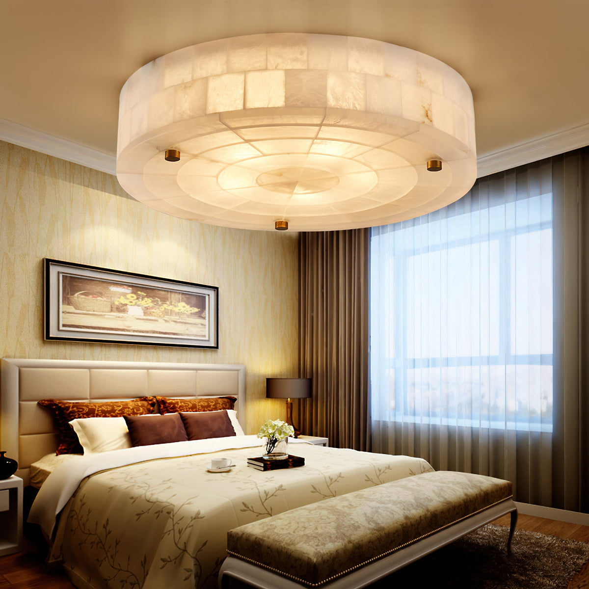 A Clérachic round alabaster ceiling light lit warm above a bed with gold bedding, a tufted headboard and sheer curtains.